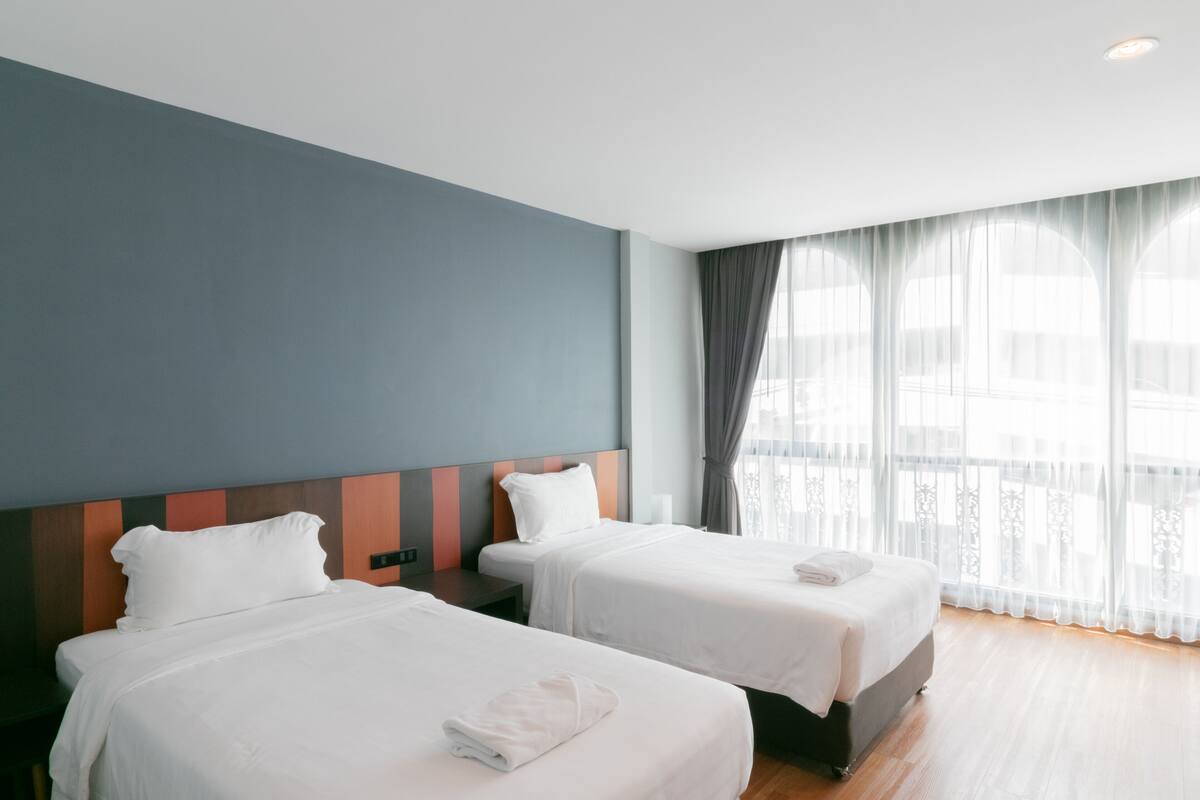 Une chambre d’hôtel avec deux lits, une grande fenêtre avec des rideaux légers et une vue sur la ville.