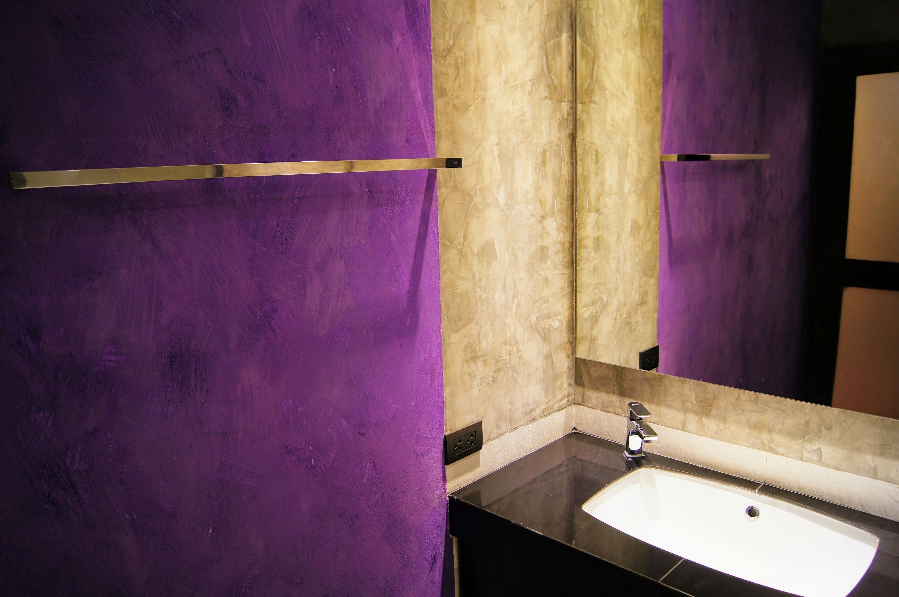 A bathroom with a purple wall, a beige tiled wall, a black countertop, and a white sink.