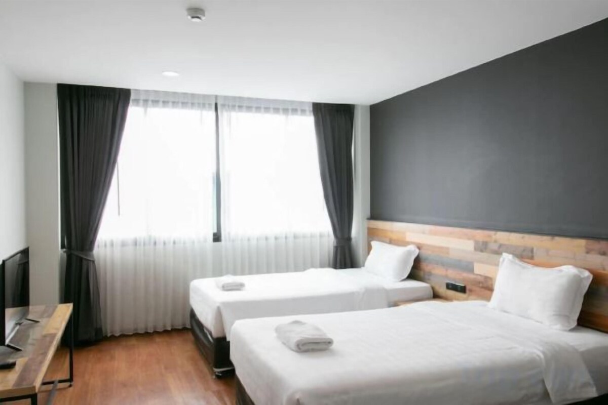 Habitación de hotel con dos camas, un escritorio y un gran ventanal con cortinas.