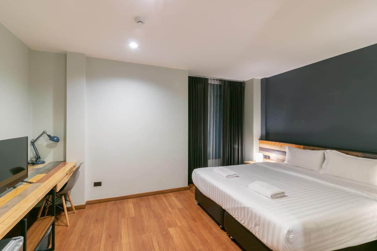 Une chambre d’hôtel moderne avec un bureau en bois, un grand lit et un mur d’accent de couleur sombre.