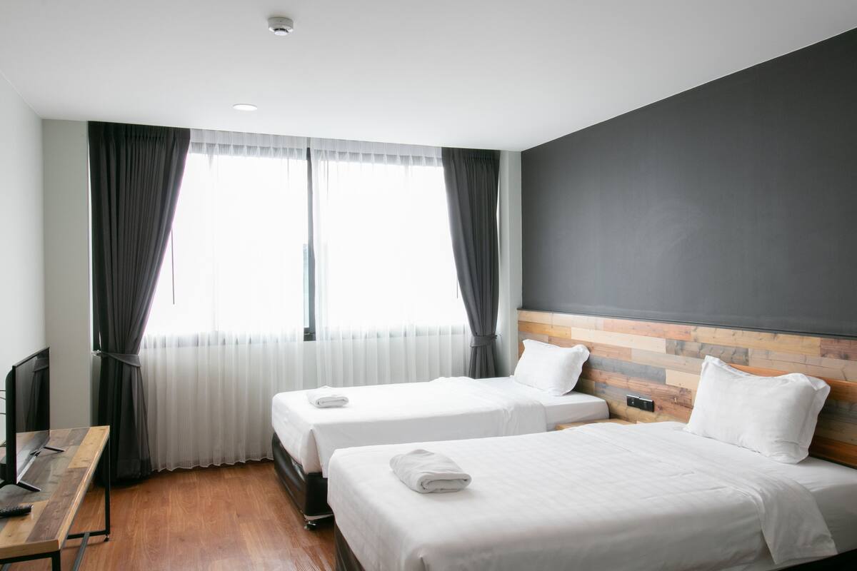 Une chambre d’hôtel avec deux lits, un bureau en bois et une grande fenêtre avec des rideaux.