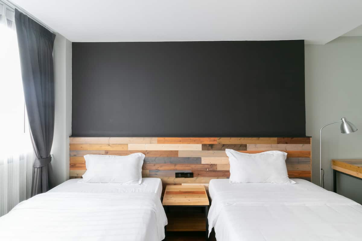 Une chambre d’hôtel avec deux lits, une tête de lit en bois, un grand mur de couleur sombre et une fenêtre avec des rideaux.