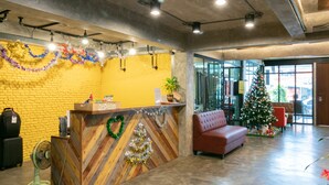 Un espace d’accueil avec un comptoir de réception en bois, un canapé rouge, un sapin de Noël et un ventilateur.
