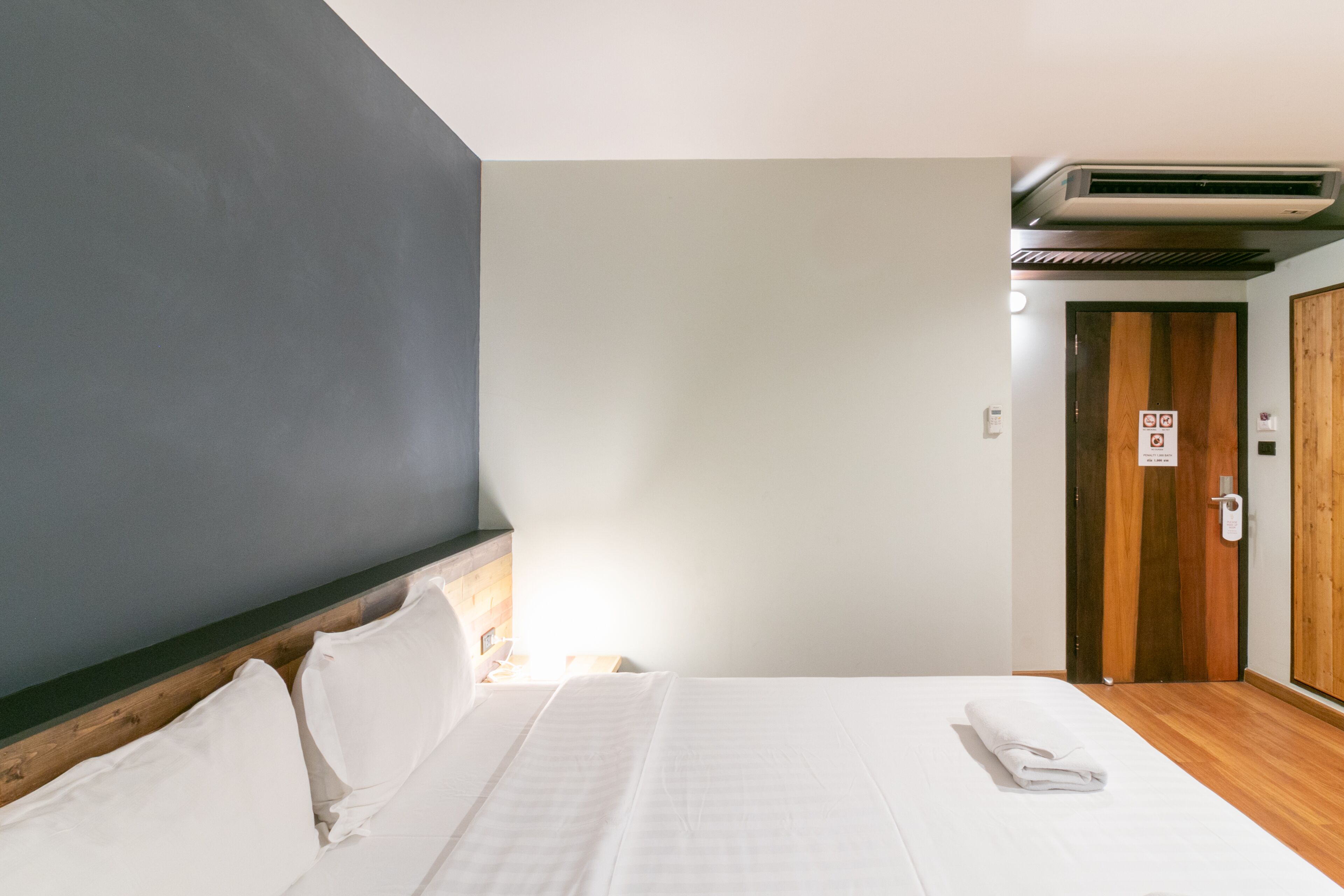 Hotelkamer met een bed, een houten hoofdbord, een wandairconditioner en een deur met een bordje.