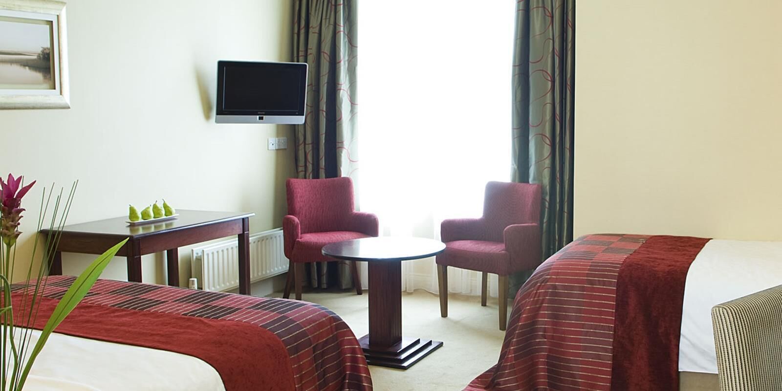 A hotel room with two beds, a TV, a small table, two chairs, and a view of the outdoors.