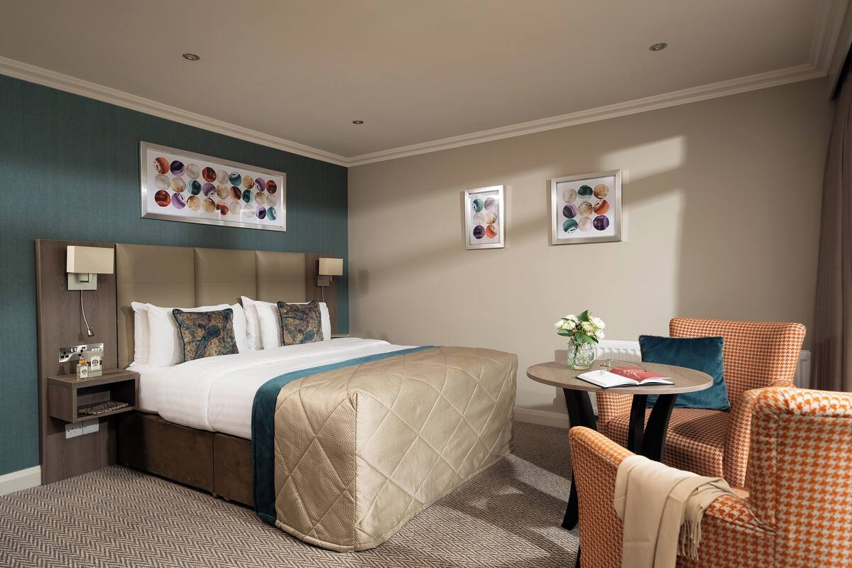 Une chambre d’hôtel avec un lit, une table de chevet, une table avec un livre et des fleurs, et deux chaises.