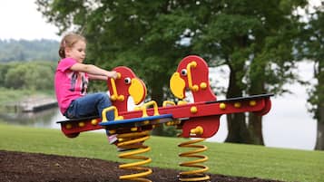 A child playing on a seesaw with a lake and trees in the background.