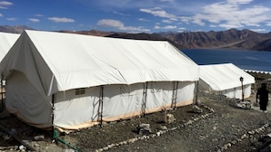 Une rangée de tentes blanches, avec un sol rocheux et des montagnes en arrière-plan.
