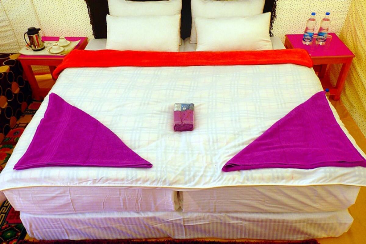 A bed with a red blanket, two purple towels, and a small item in the center.