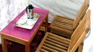 Une petite table en bois avec un plateau rose, une cafetière en métal et une assiette sur laquelle se trouve une tasse.