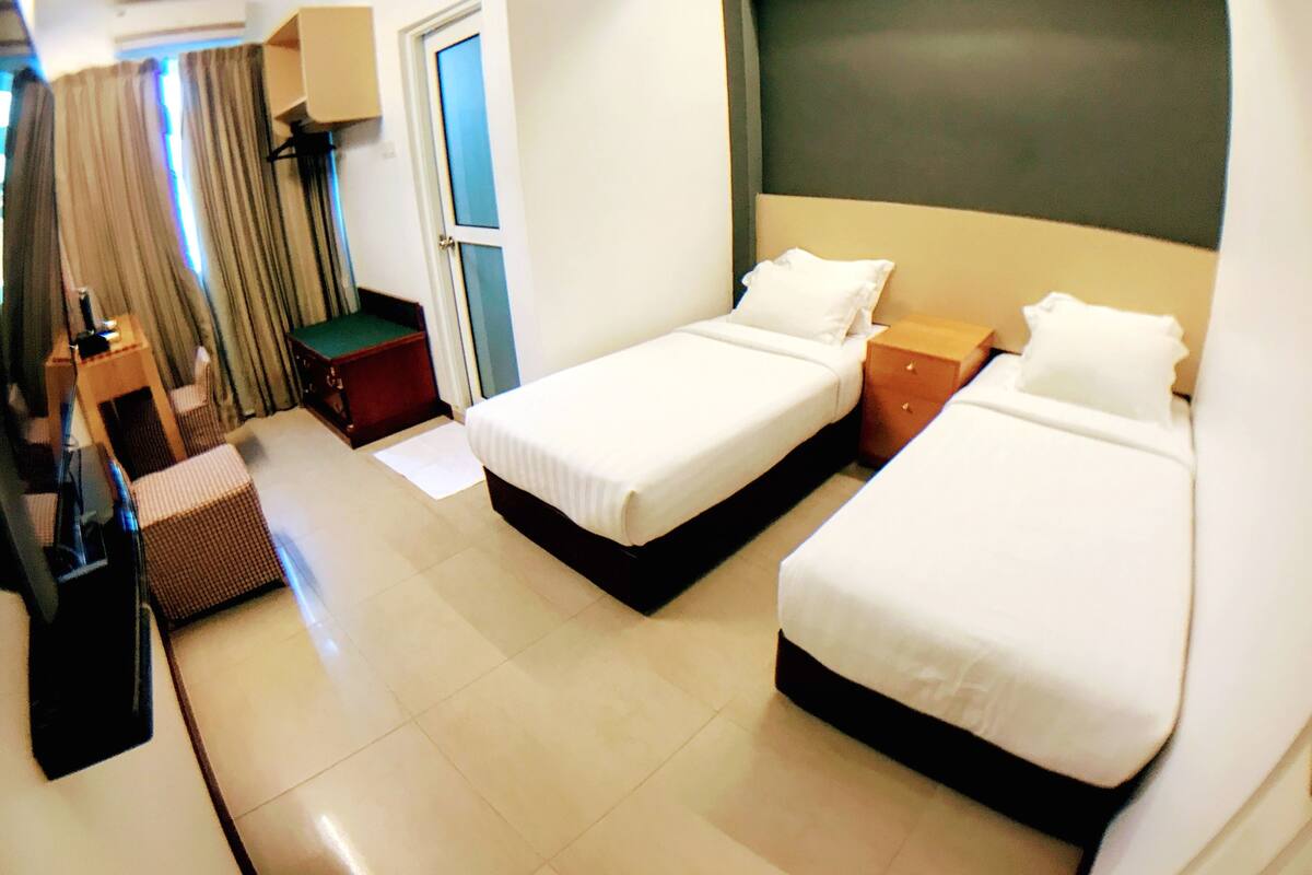 A hotel room with two single beds, a desk, a chair, a small table, and a door.