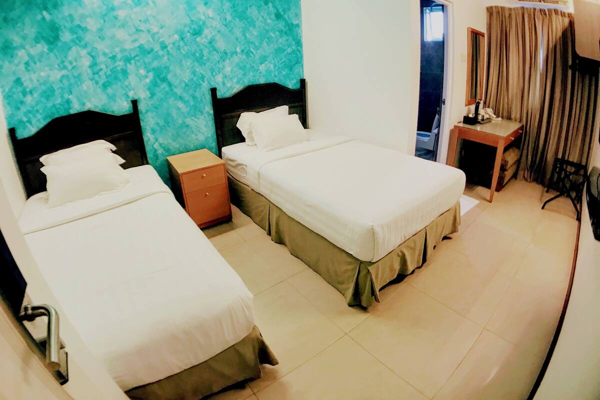 A hotel room with two beds, a small table, a chair, and a window with curtains.