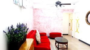 A living room with a red sofa, a small round table, and a ceiling fan. - Lux Private Hotel (Petaling Jaya)