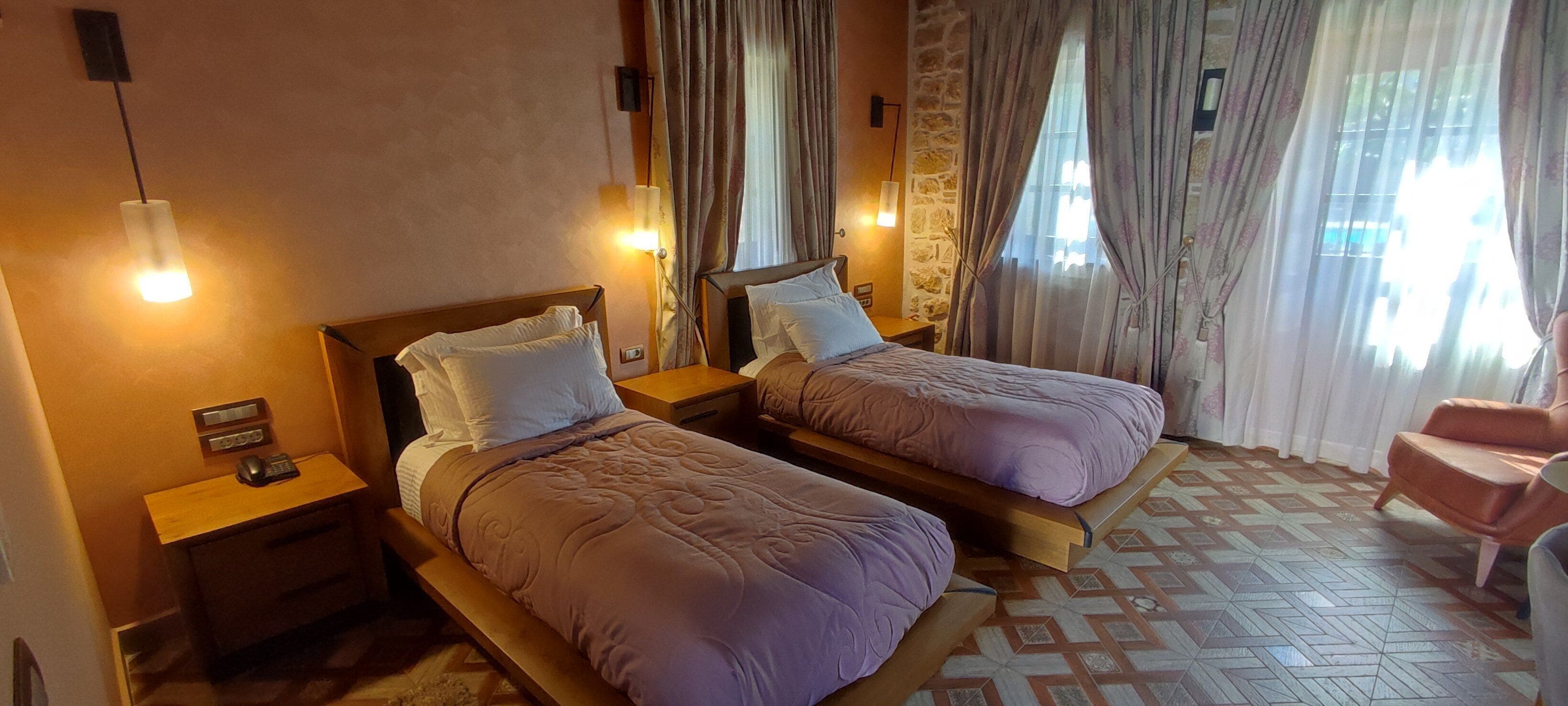 A hotel room with two beds, a wooden nightstand with a phone and a remote, a chair, and a patterned floor.