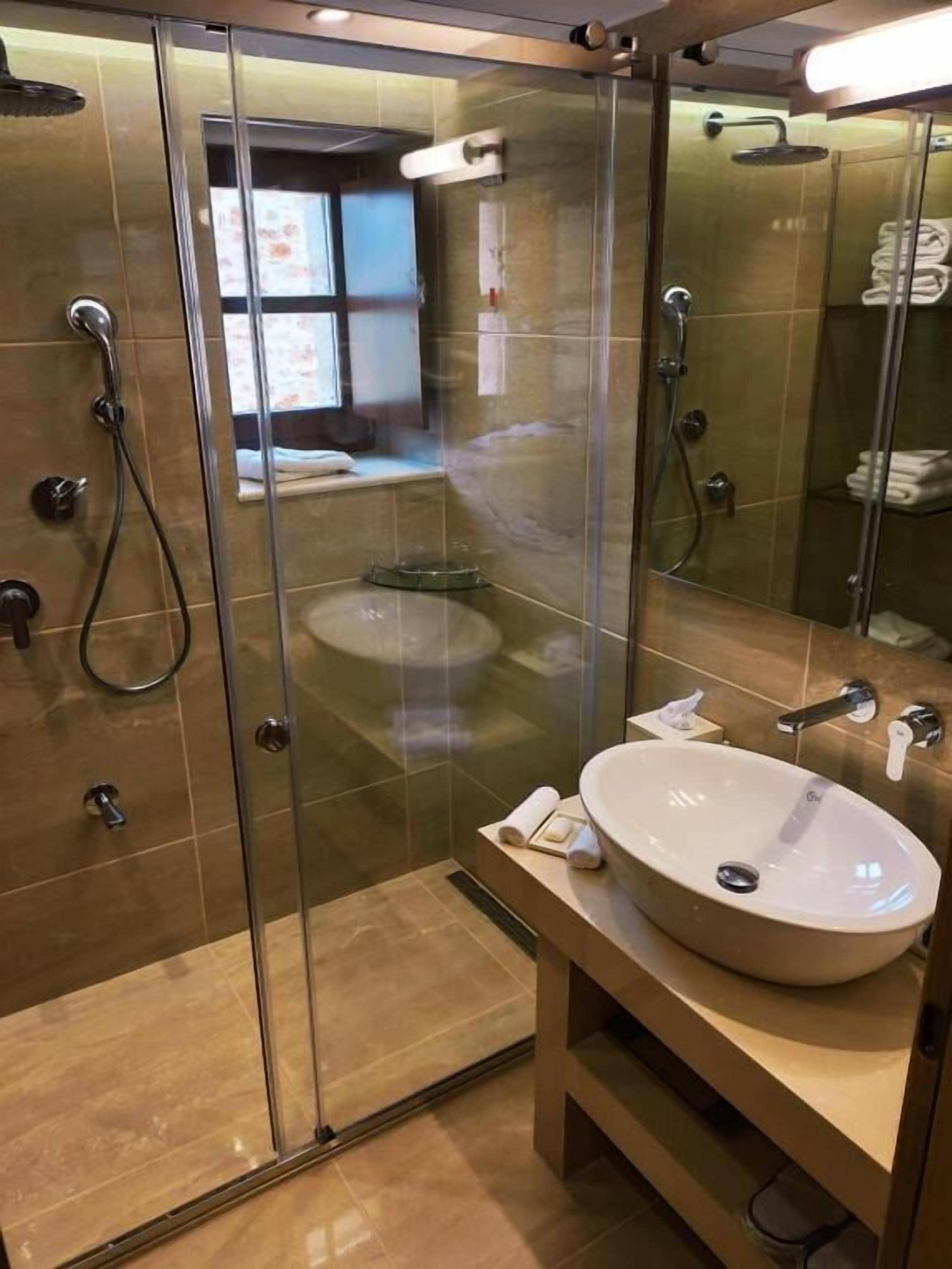 Un baño moderno con ducha de vidrio, un lavamanos espacioso y una bañera a la vista al fondo.