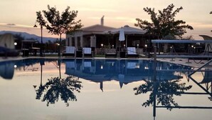 A swimming pool with lounge chairs and umbrellas, surrounded by trees and a building with a dome roof. - Mystras Grand Palace Resort & Spa (Sparta)