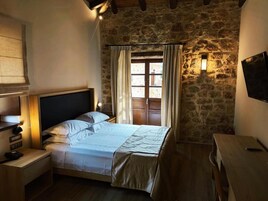 Un dormitorio con pared de piedra, una cama con cabecera de madera, una mesita de noche con lámpara y una ventana con cortinas.