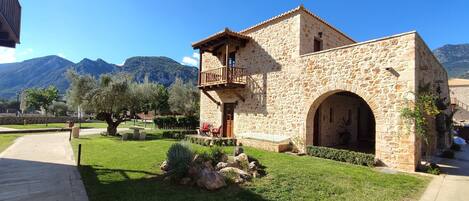 Un edificio de piedra con balcón, arco y jardín con rocas y árboles.