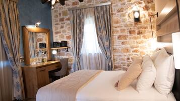 Quarto com parede de pedra, escrivaninha de madeira e cama com roupa de cama branca.