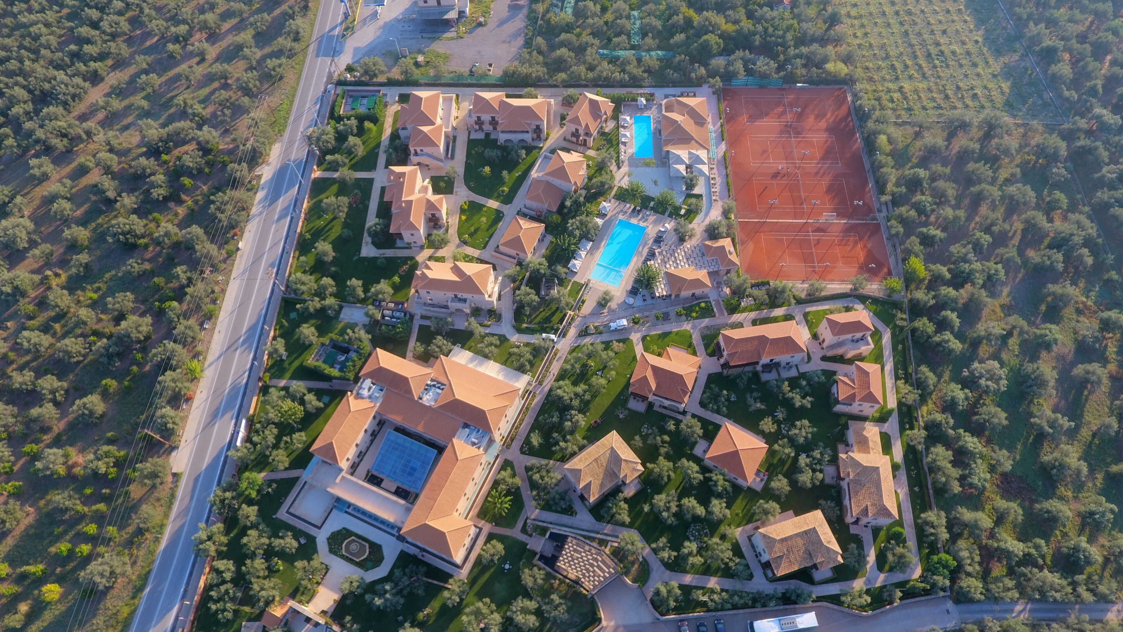 An aerial view of a residential area with multiple houses, a swimming pool, tennis courts, and a large open field.