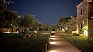 A nighttime view of a paved pathway flanked by trees and stone buildings, with lights illuminating the path. - Mystras Grand Palace Resort & Spa (Sparta)