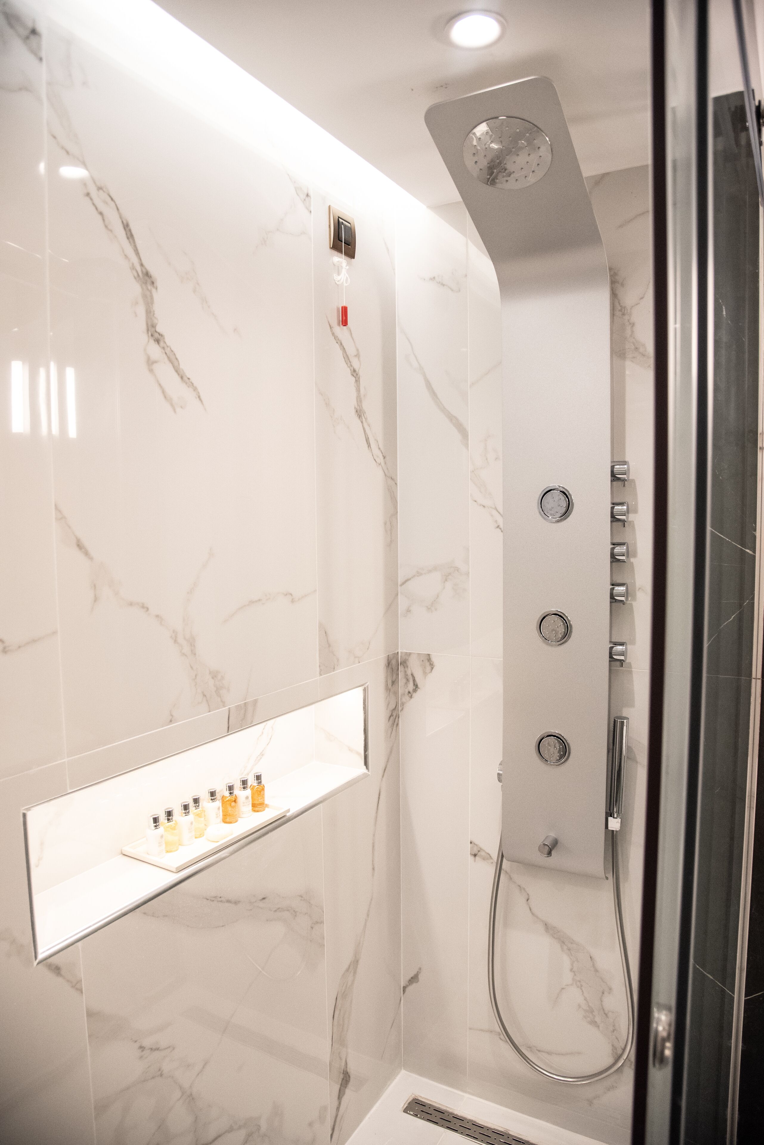 Eine moderne Dusche mit Glasabtrennung, Marmorwänden und einem integrierten Ablagebereich für Toilettenartikel.