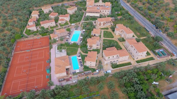 An aerial view of a residential area with multiple stone buildings, a tennis court, and a swimming pool. - Mystras Grand Palace Resort & Spa (Sparta)