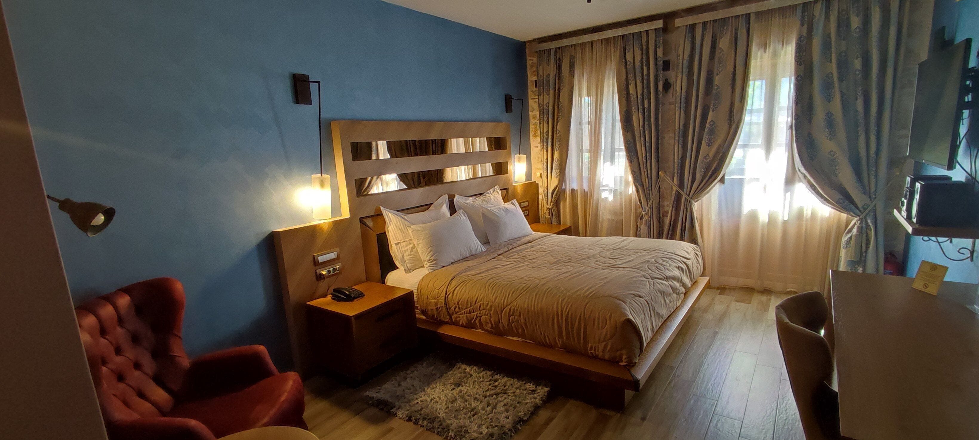 A hotel room with a bed, bedside table, lamp, chair, and a desk with a chair.