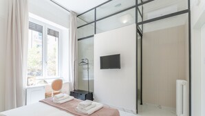 Habitació d'hotel amb llit, televisió, dutxa i escriptori amb cadira.