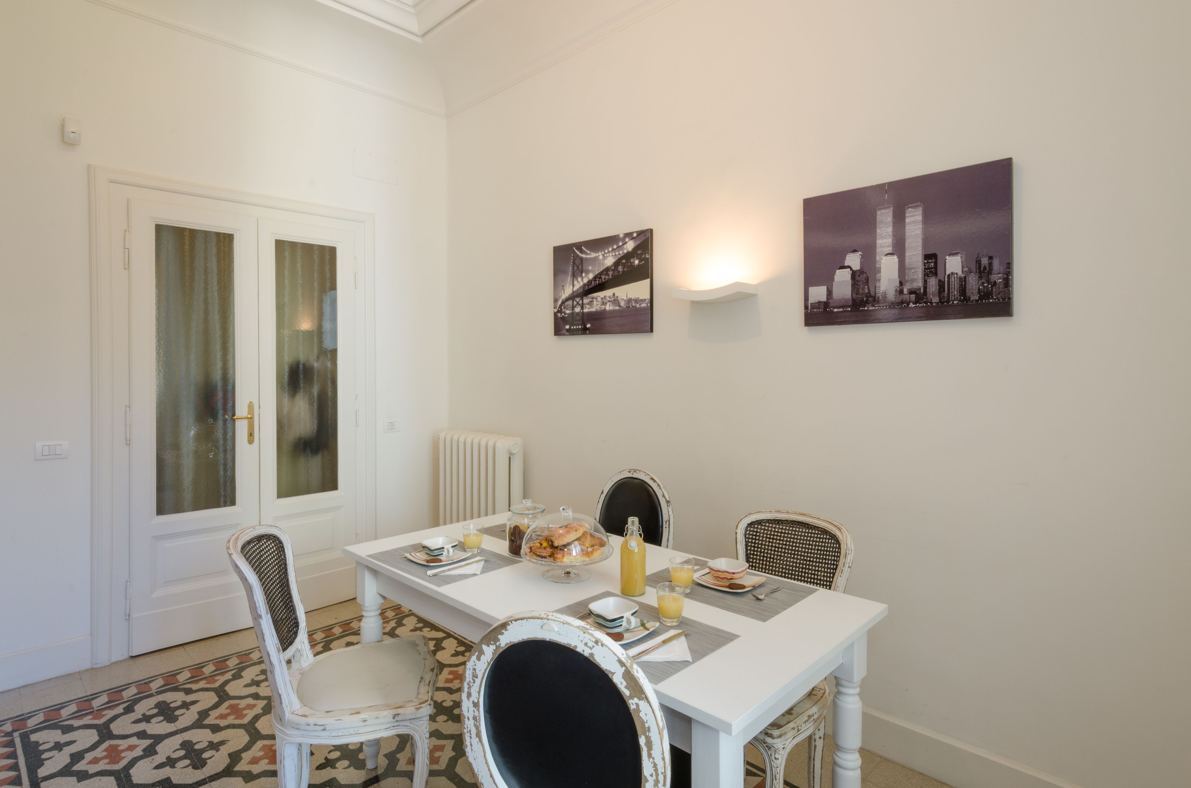 Un comedor con una mesa blanca, cuatro sillas y dos lámparas fijadas a la pared.