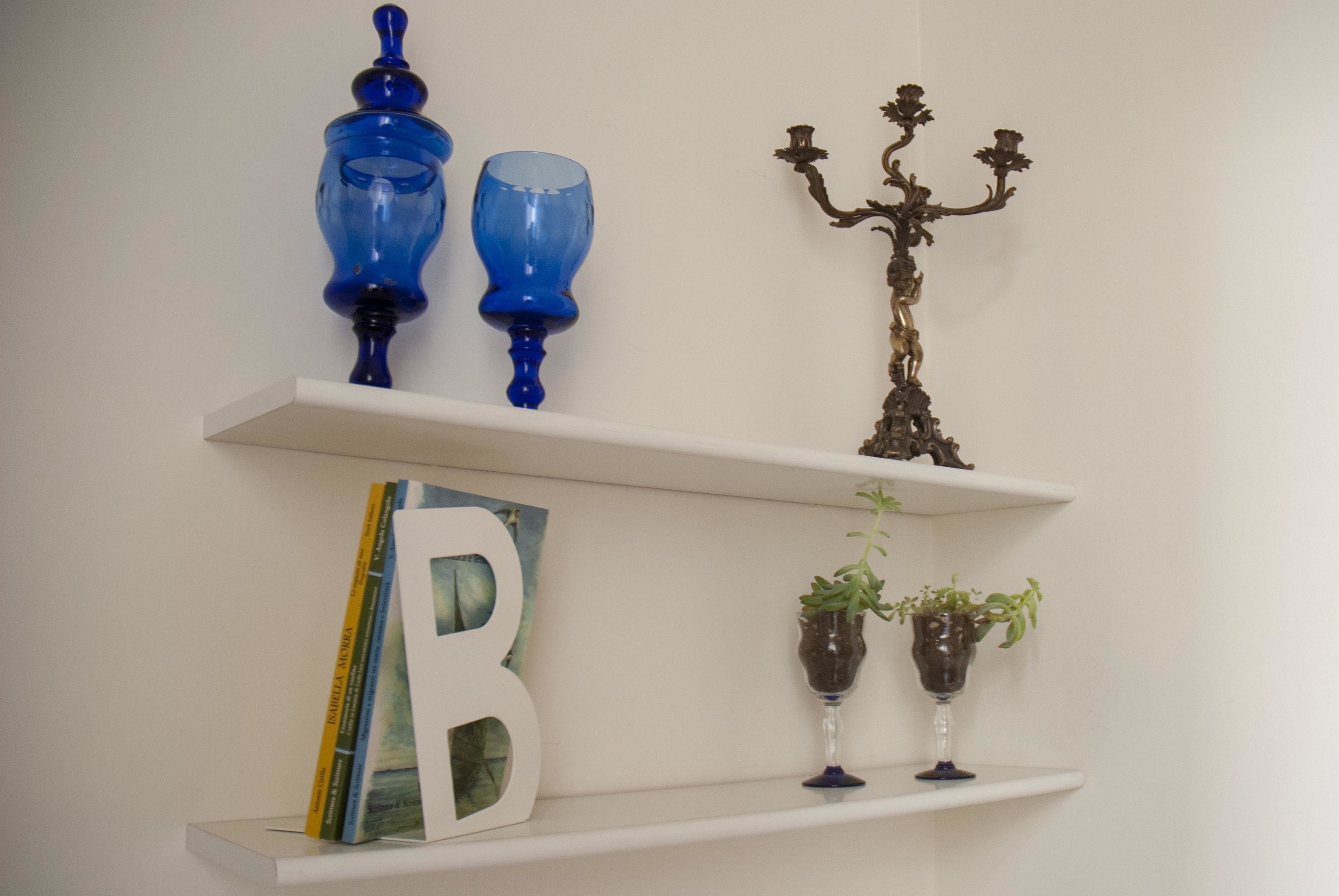 Uno scaffale con oggetti decorativi, tra cui un vaso blu, un candelabro e la lettera 'B'.