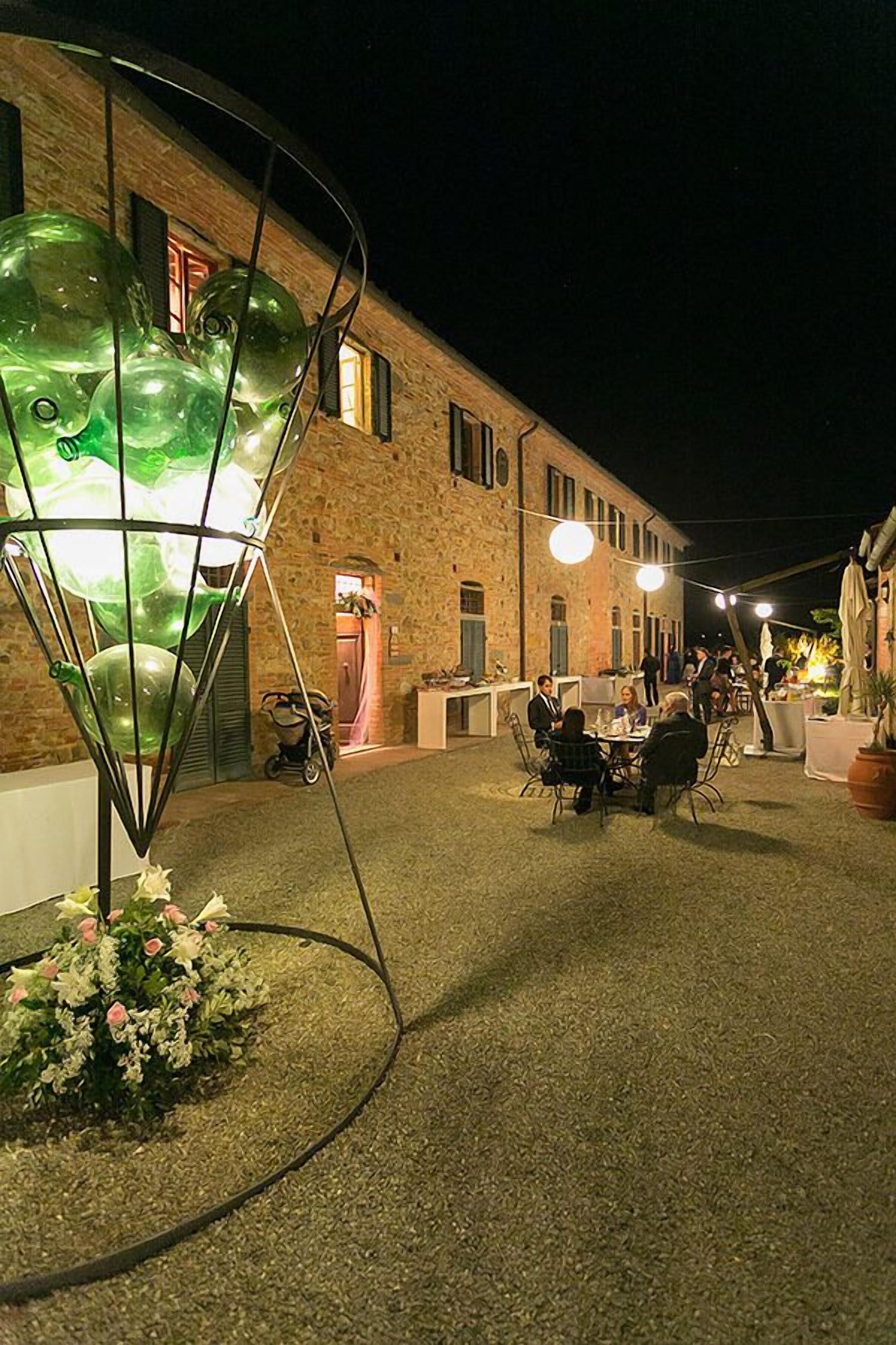 Un'area esterna con tavoli e sedie, un edificio in mattoni, e una scultura in vetro verde.