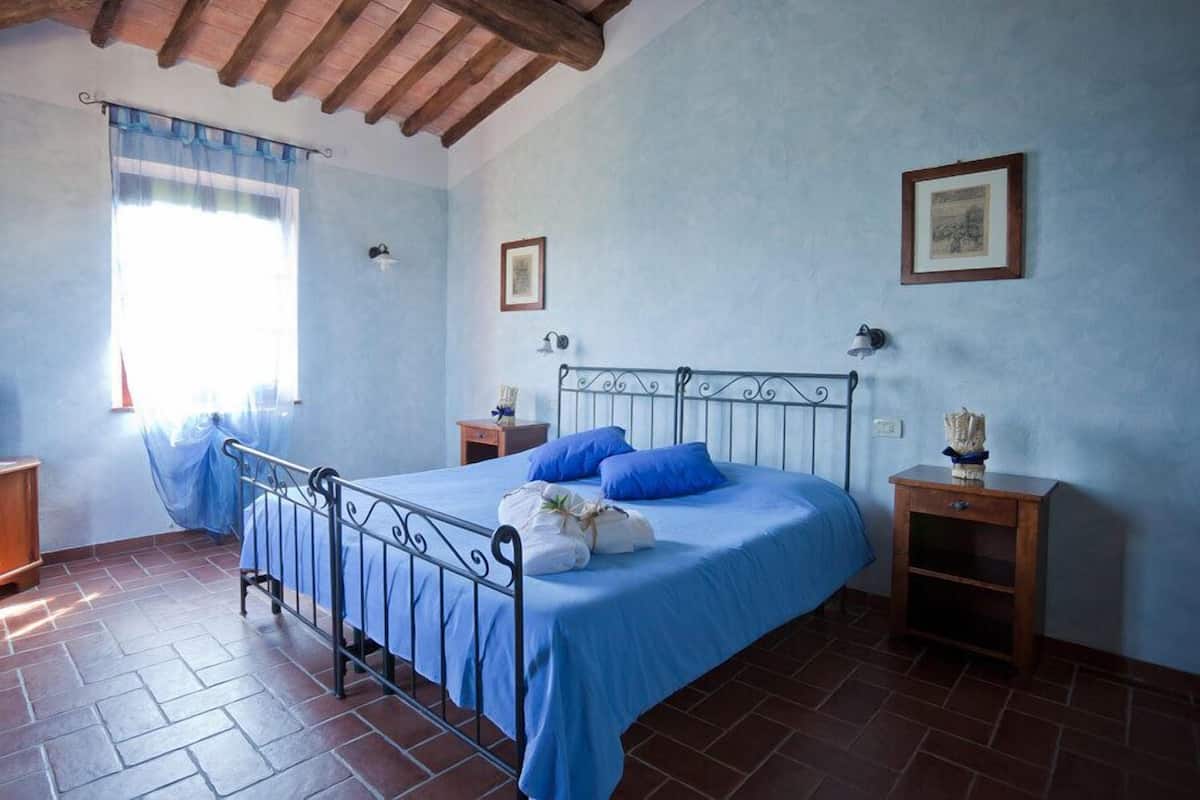 A bedroom with a metal bed frame, blue bedding, a wooden nightstand, and a window with a blue curtain.