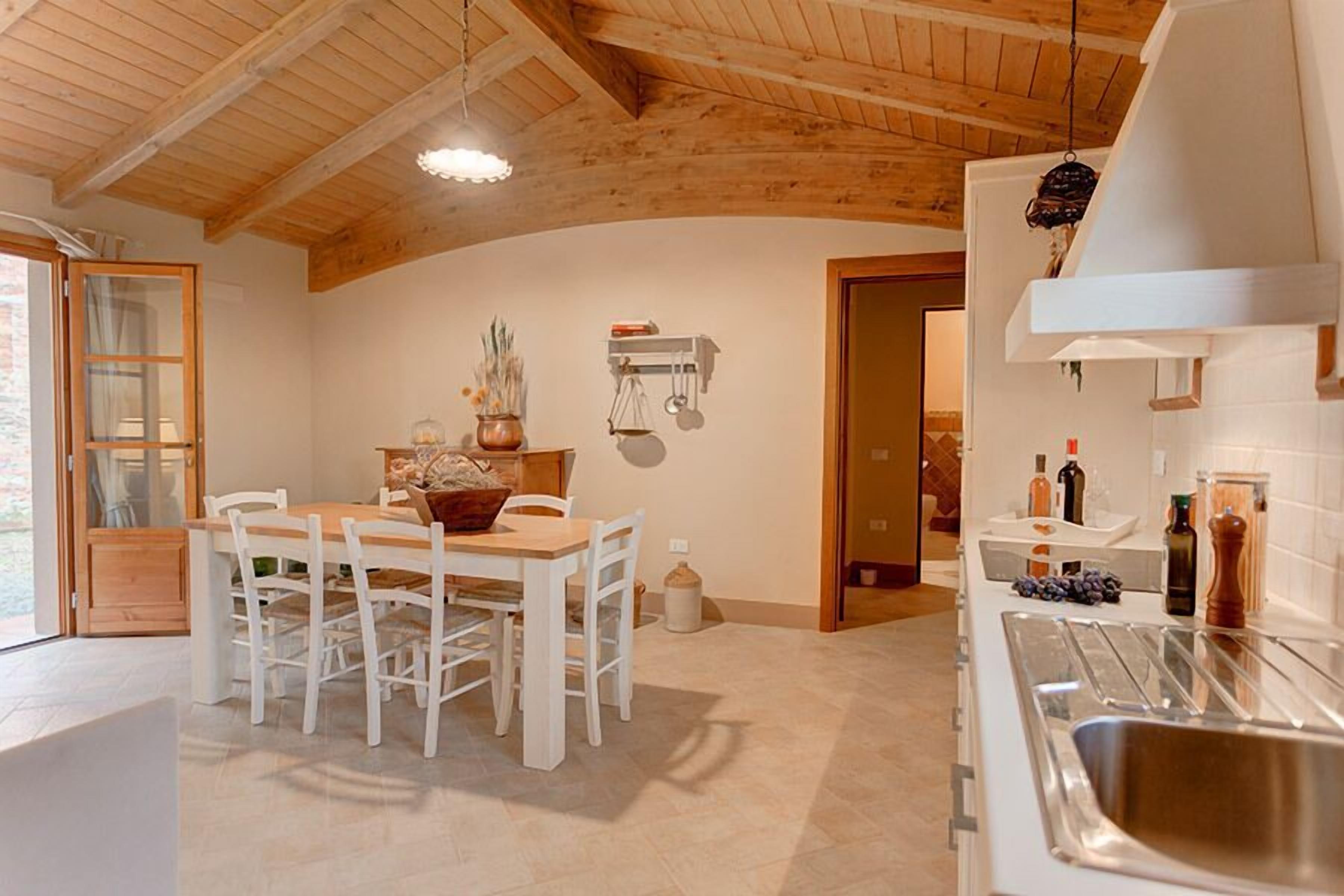 A kitchen with a wooden ceiling, white walls, a dining table with chairs, and a modern sink.