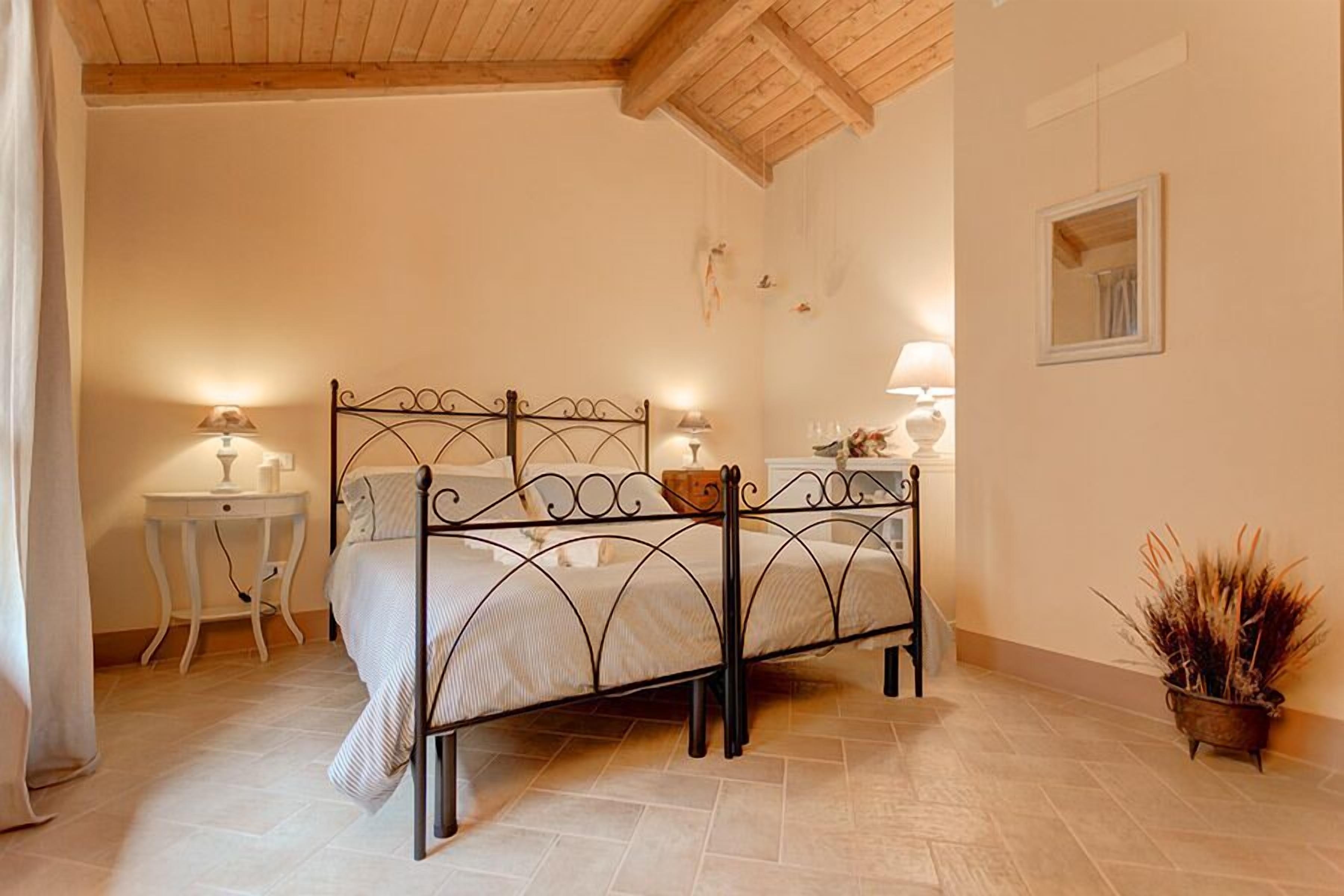 A bedroom with a metal bed frame, a bedside table with a lamp, a small bedside table with a lamp, and a potted plant.
