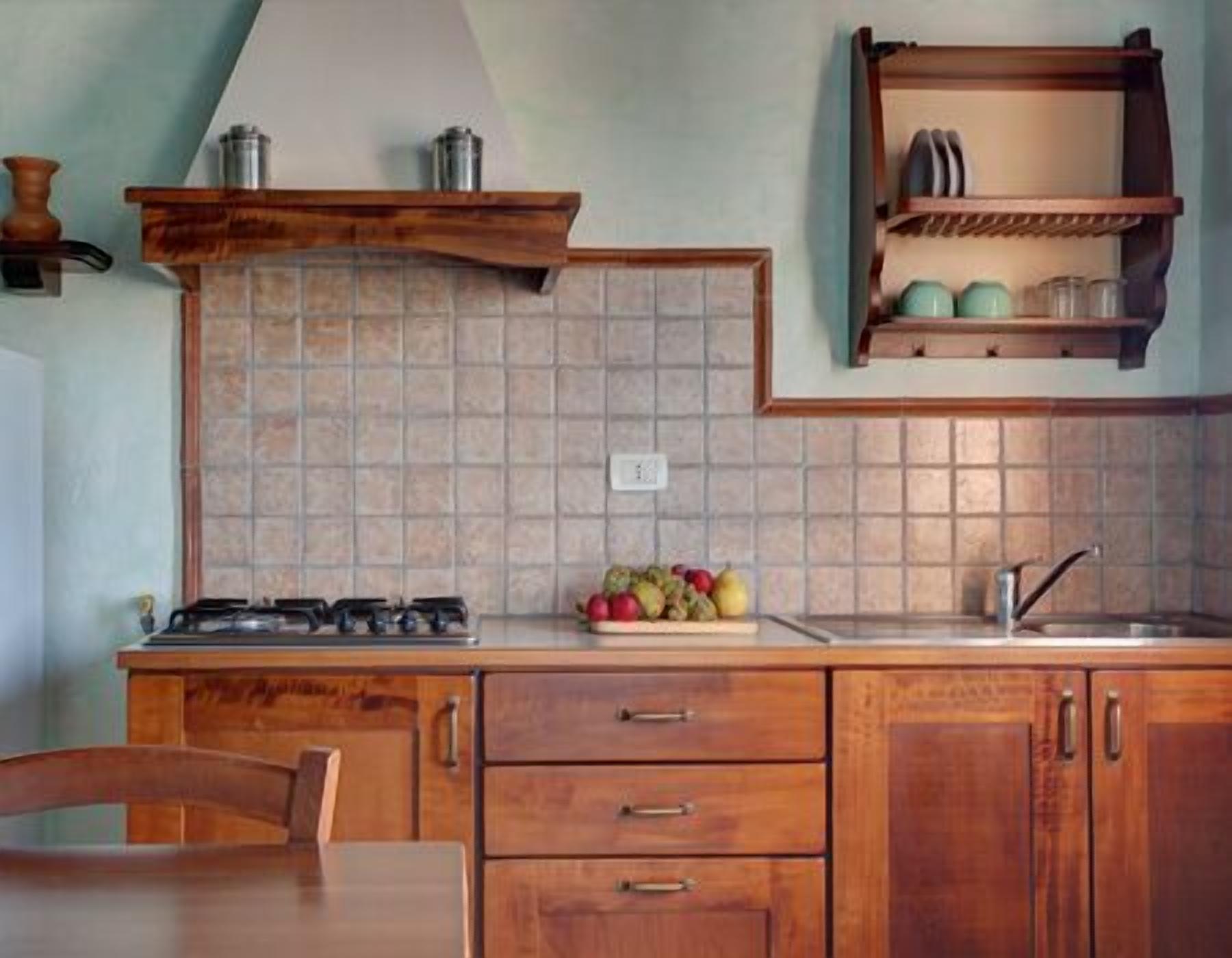 Uma cozinha com armários de madeira, fogão a gás, painel de azulejos e uma fruteira sobre o balcão.