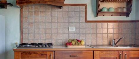 Uma cozinha com armários de madeira, fogão a gás, painel de azulejos e uma fruteira sobre o balcão.