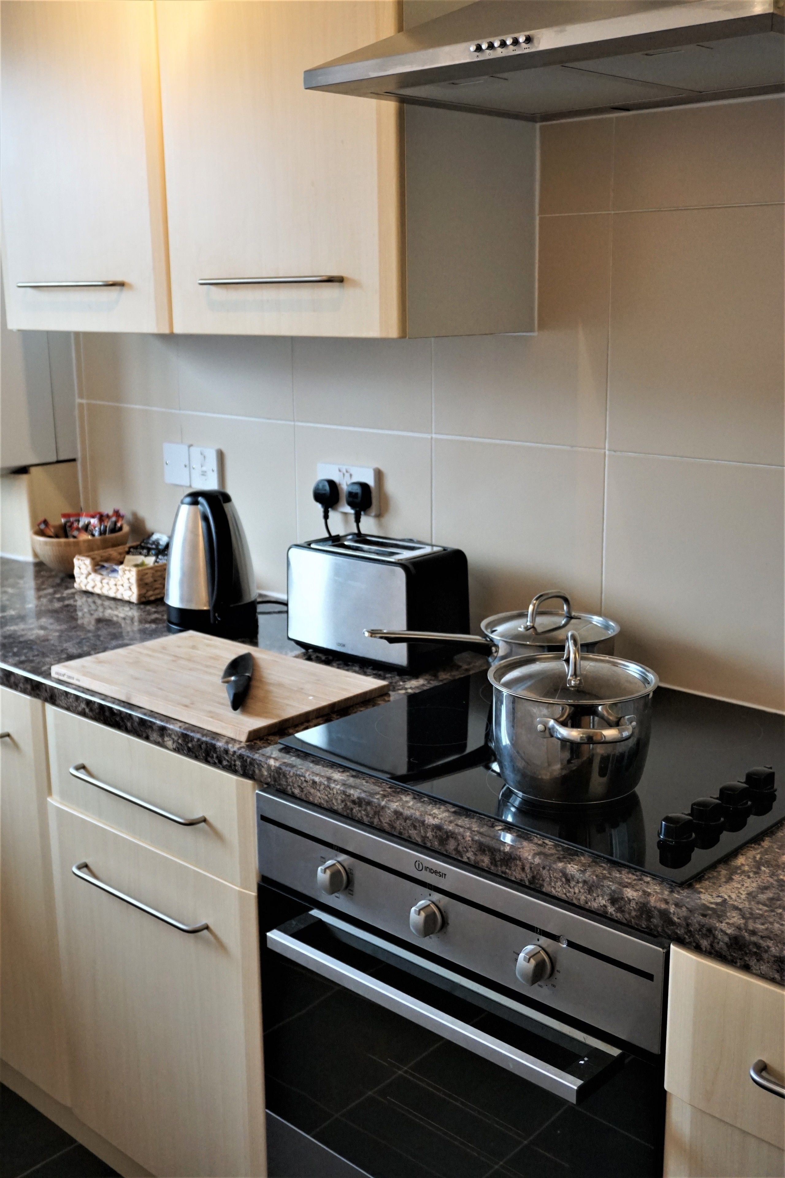 A kitchen with a toaster, a kettle, and a pot on the counter. There are cabinets and drawers with handles.