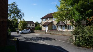 Une rue résidentielle bordée de maisons, avec une voiture garée et un ciel bleu dégagé.