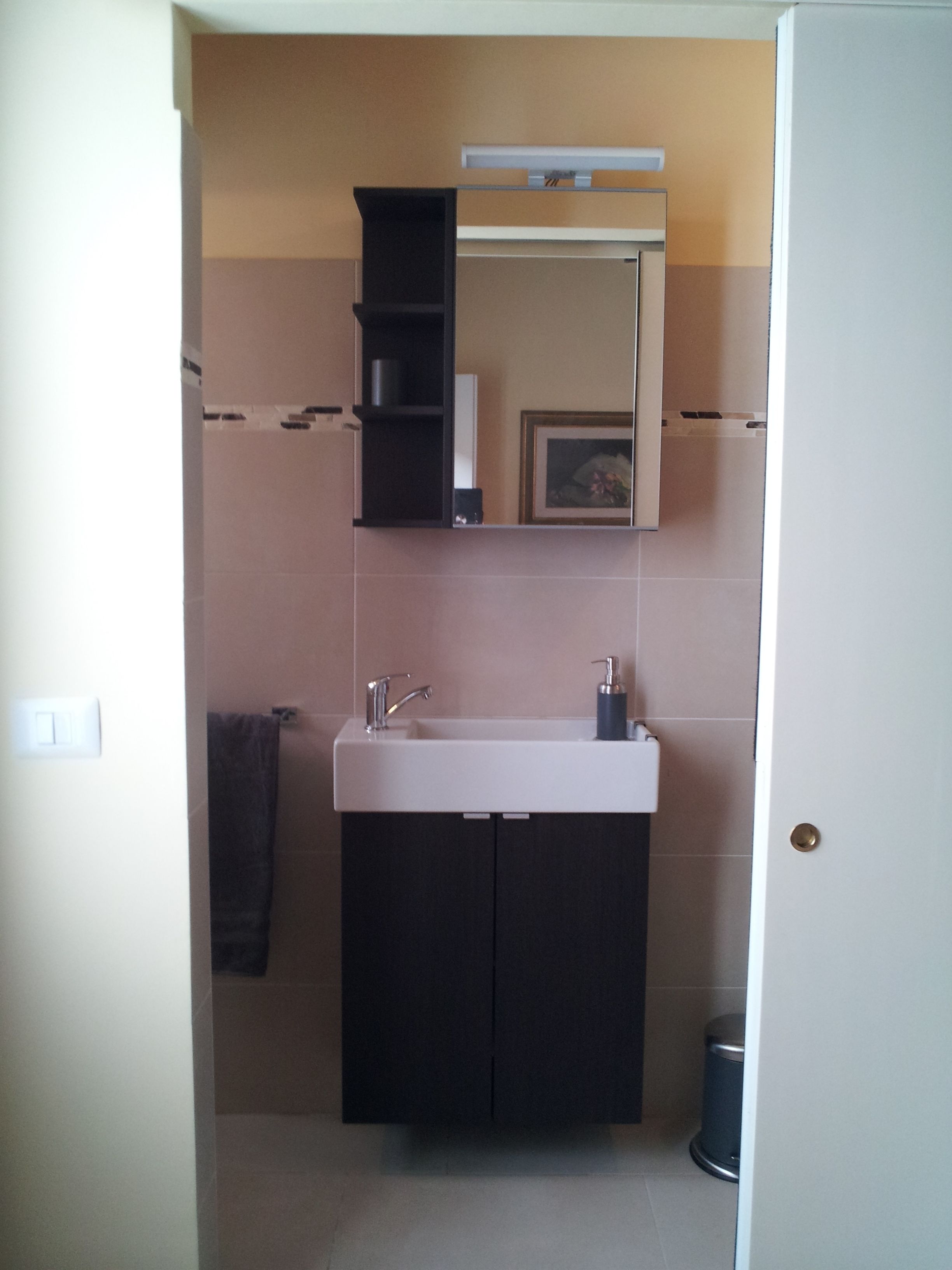 Een badkamer met een witte wastafel, donkere kastjes, een spiegel en een prullenbak.