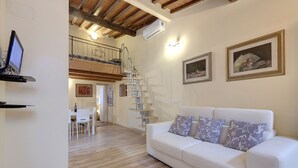 A spacious living area with a white sofa, a dining table with chairs, a staircase, and a ceiling with exposed beams. - Monna Lisa Apartment (Florence)