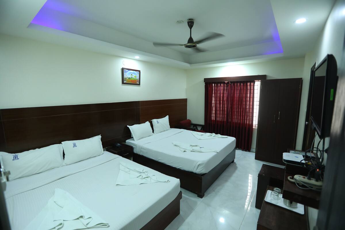 A hotel room with two beds, a ceiling fan, a desk with a computer, and a TV.