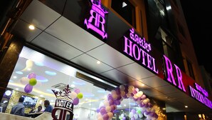 A hotel entrance with a neon sign, a reception desk, and a glass facade. - Hotel RR International (Bengaluru)