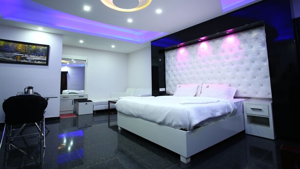 A modern bedroom with a white bed, a tufted headboard, and a bedside table. - Hotel RR International (Bengaluru)