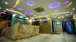 A hotel reception area with a marble reception desk, a digital screen, and a Pepsi advertisement. - Hotel RR International (Bengaluru)