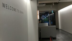 Un interior moderno con un letrero que dice 'WELCOME TO OSAKA', un mostrador de recepción y un separador de vidrio.