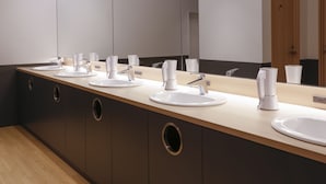 Un baño moderno con un lavabo largo, varios lavamanos y un espejo grande.