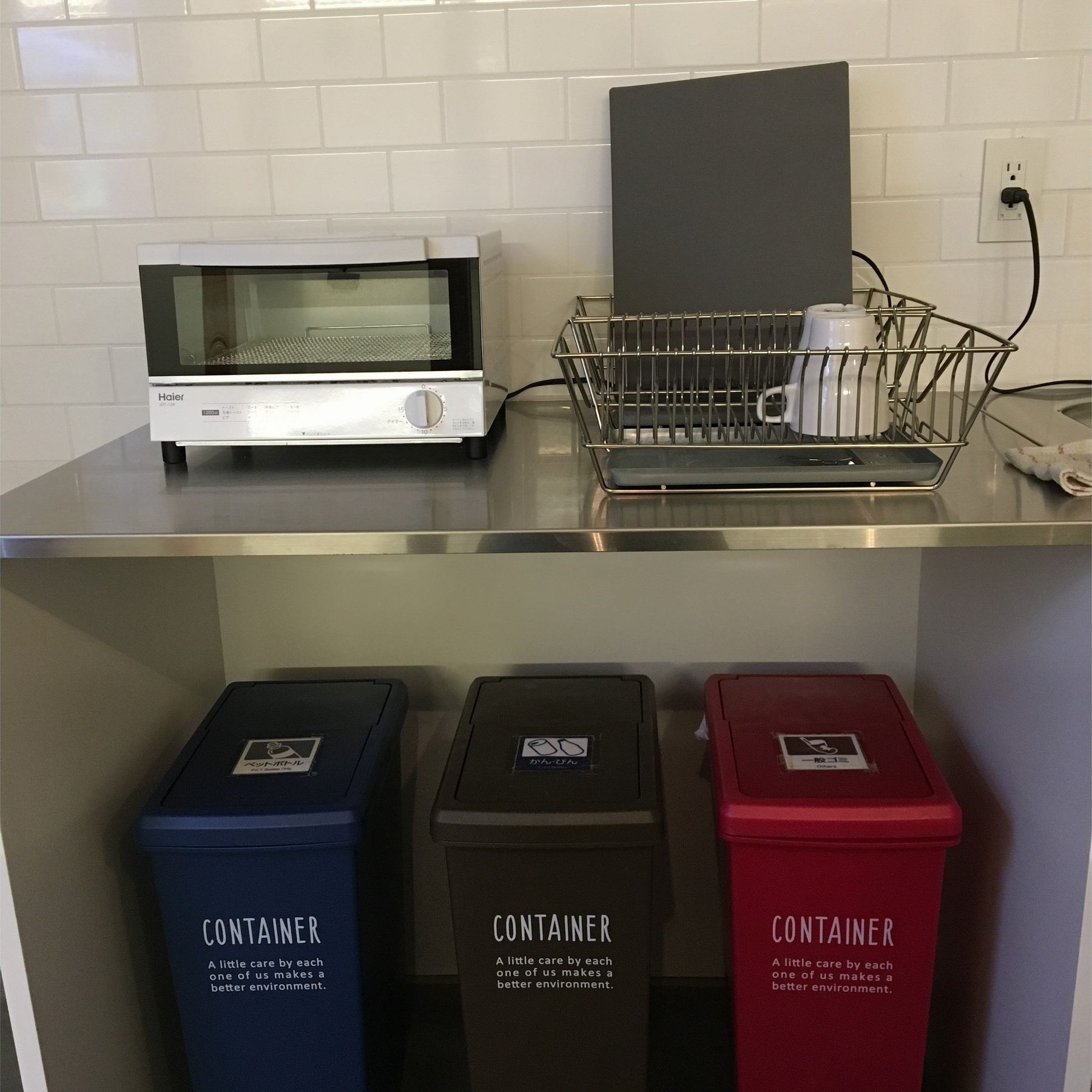 Eine Küchenzeile mit einem Toaster, einem Geschirrgestell und drei Behältern zur Mülltrennung.