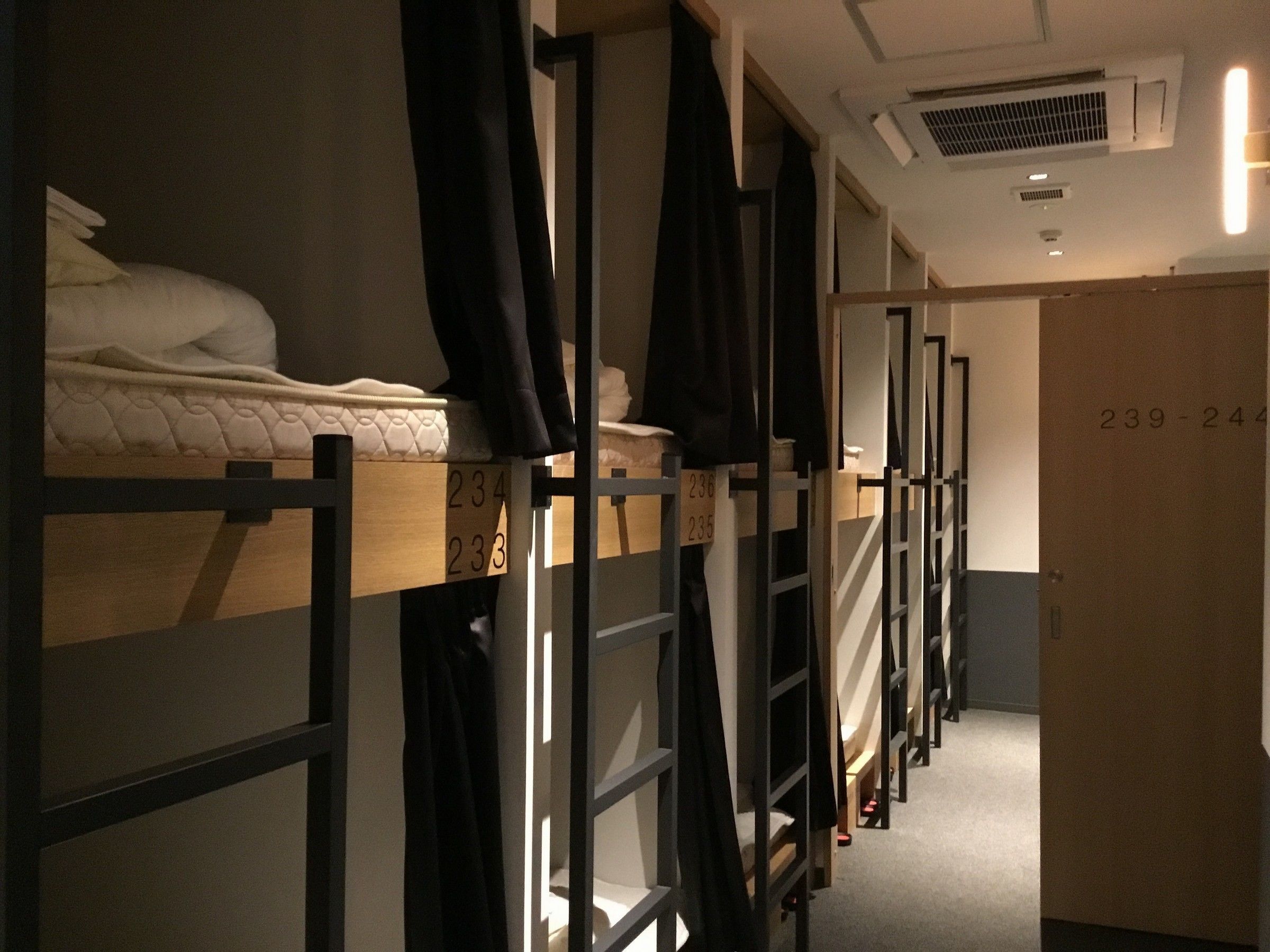 A dormitory room with bunk beds, a wooden ladder, and a door with numbers.