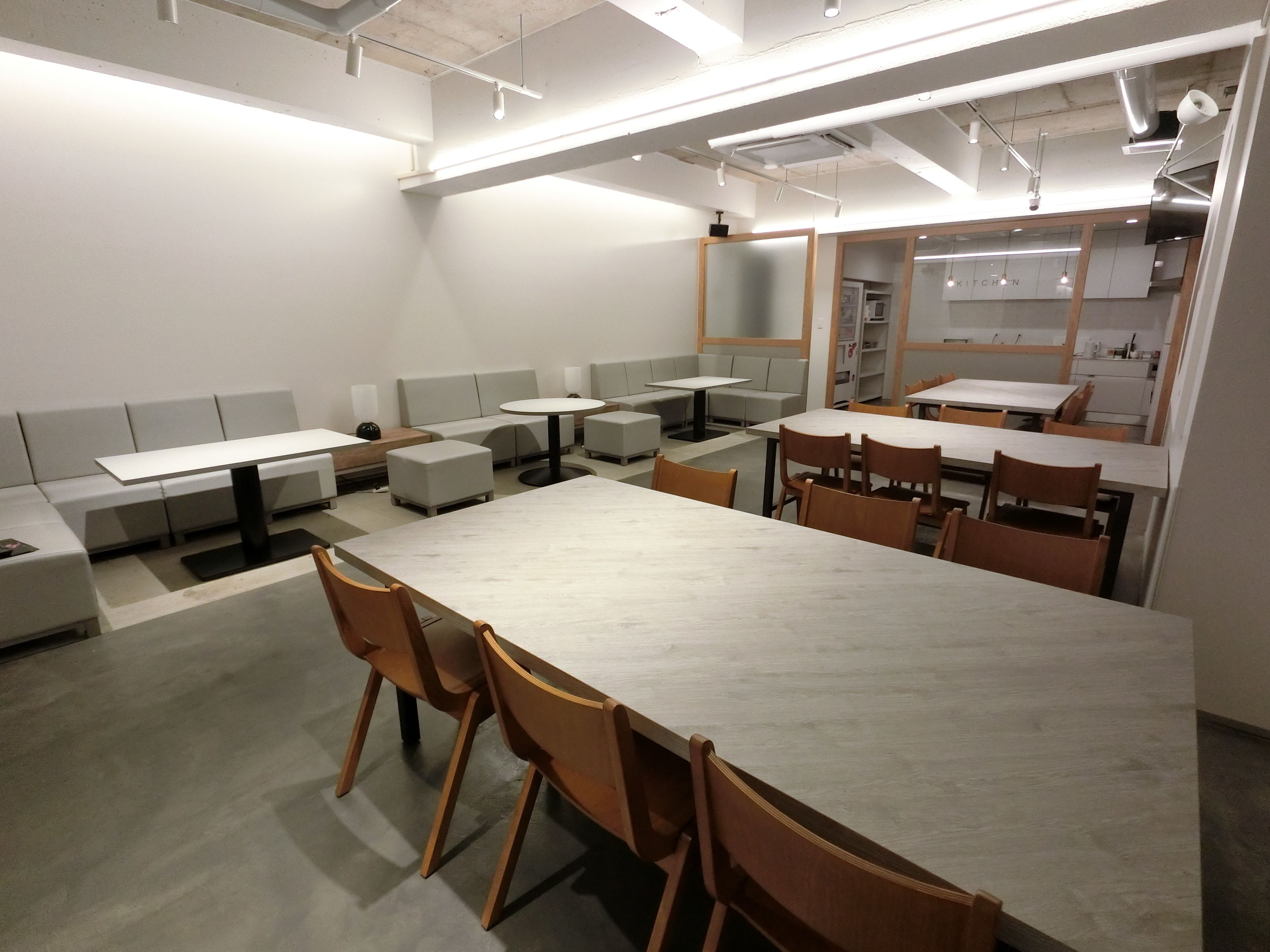 A modern dining area with high tables and benches, a kitchen in the background, and a clean, minimalist design.